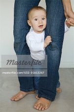 632-01613267em-Baby-standing-between-parent's-legs-looking-at-camera.jpg